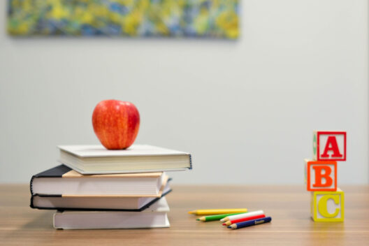 Stack of books with an apple, toy blocks spelling ABC, and colored pencils on a desk