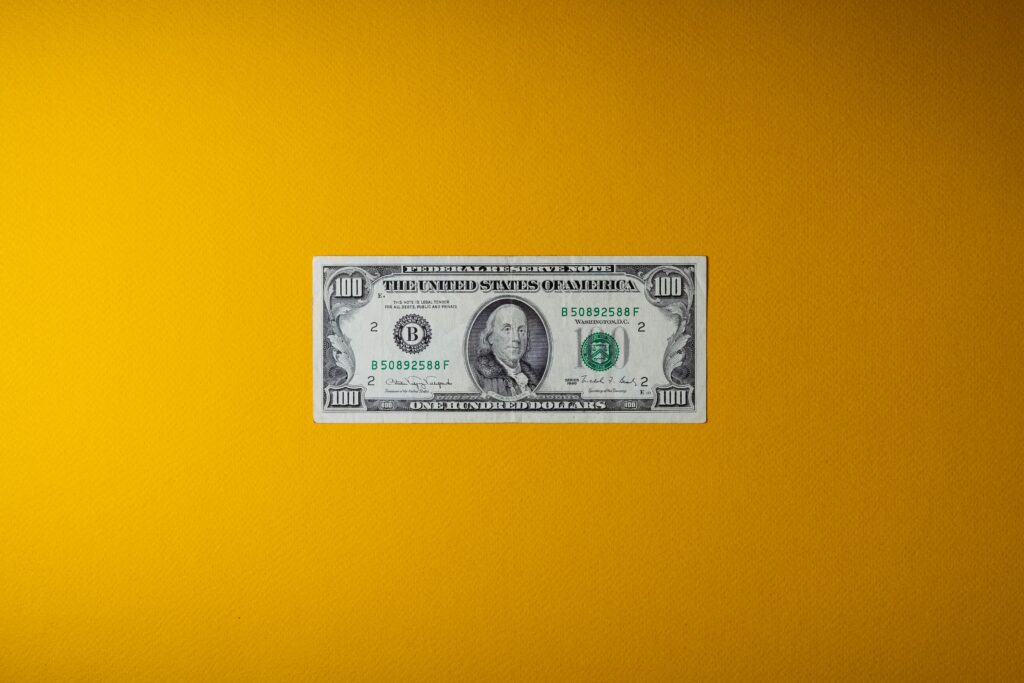 A $100 bill centered on a vibrant yellow background, featuring Benjamin Franklin's portrait. The image conveys a vivid, bold mood.